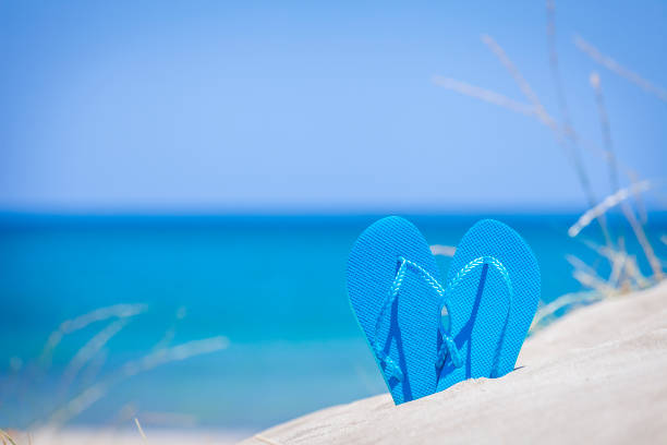 Summer, beach or holiday backgrounds: blue flip flops on white sand dune