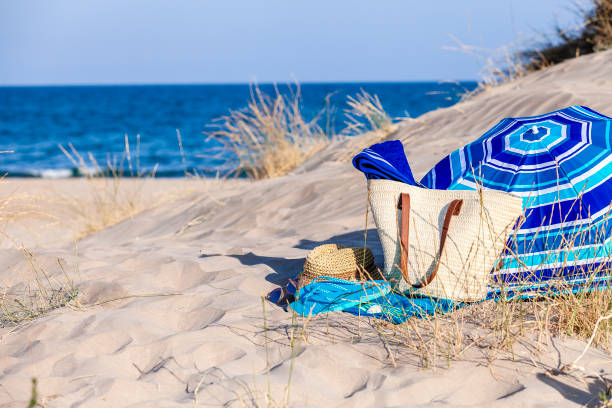 Beach, summer or holidays backgrounds concept. Horizontal view of blue beach accessories on white sand dune against defocused blue ocean background. Beach accessories included in the composition are a beach bag, sun hat, beach umbrella, two beach towels, a pair of flip flops ans sunglasses. The composition at the right of the frame leaving useful copy space for text and/or logo. Predominant colors are blue and white. DSRL outdoors photo taken with Canon EOS 5D Mk II and Canon EF 24-105mm f/4L IS USM Wide Angle Zoom Lens
