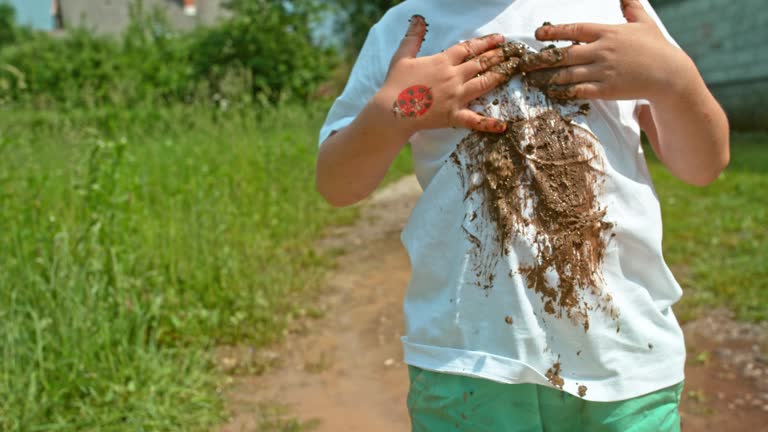 SLO MO Little boy putting mud on his white t shirt while standing in the muddy puddle