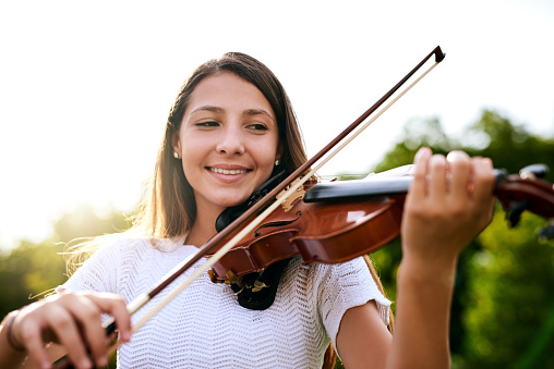 Shot of a cheerful young girl playing the violin while standing in the backyard of her home during the day