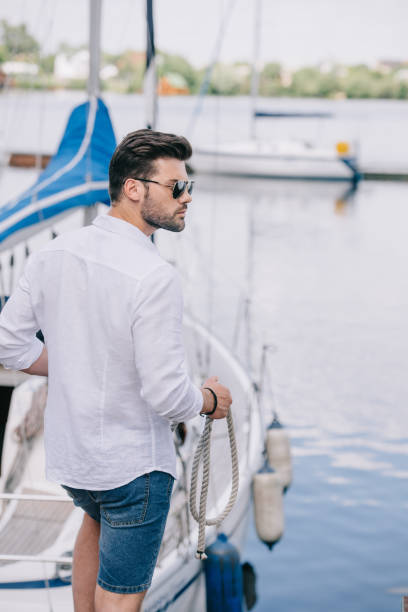 istock handsome young man in sunglasses looking away while holding rope at yacht 999149254