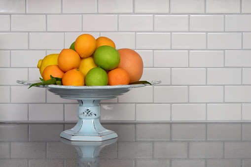 Homegrown selection of citrus fruit in retro modern kitchen with white ceramic subway tile backsplash and quartz countertop.