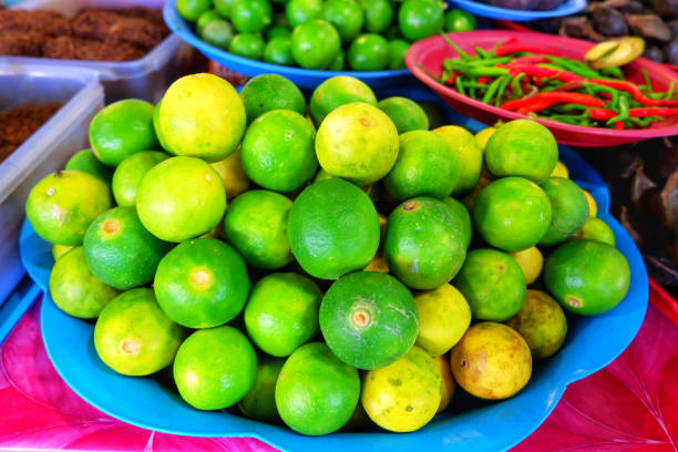 lime or green lemon on the tray in the vegetable shop in the food market. - lime market vietnam fruit imagens e fotografias de stock