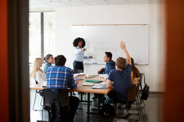 istock Female High School Tutor At Whiteboard Teaching Maths Class With Pupil Asking Question 999246750