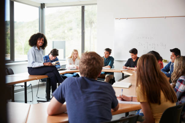 istock Female High School Tutor Sitting At Table With Pupils Teaching Maths Class 999248980