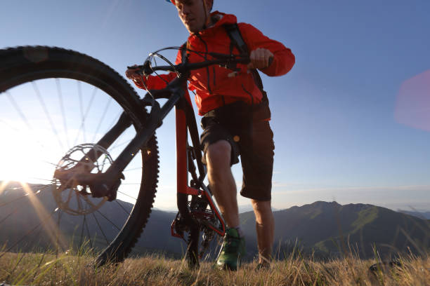 istock Mountain biker pushes bike up hill above mountains 999295394
