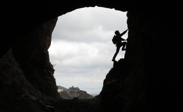 mann in einer höhle mit einer burg auf den blick klettern - spelunking stock-fotos und bilder