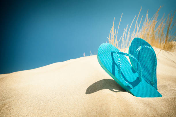 Summer or beach backgrounds: blue flip flops on gold colored sand dune