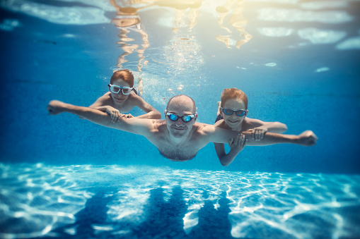Father and sons playing underwater in resort pool. Family is playing underwater superheroes.
Nikon D850
