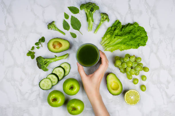 flatlay con la mano de la mujer para jugo verde rodeado de frutas verdes y vegetales en la mesa de mármol - apple women green eating fotografías e imágenes de stock