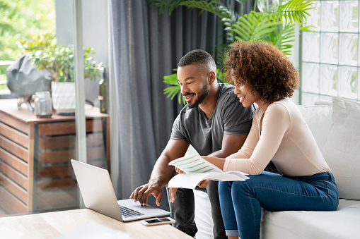 Loving African American couple paying bills online at home using a laptop computer and looking very happy - lifestyle concepts