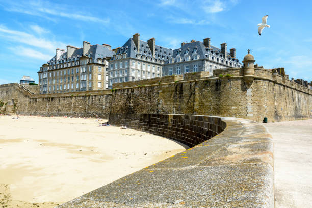 The walled city of Saint-Malo, France, with granite residential buildings protruding above the rampart and people sunbathing on the Mole beach at the foot of the high wall. The walled city of Saint-Malo, France, with granite residential buildings protruding above the rampart and people sunbathing on the Mole beach at the foot of the high wall. bailey castle photos stock pictures, royalty-free photos & images