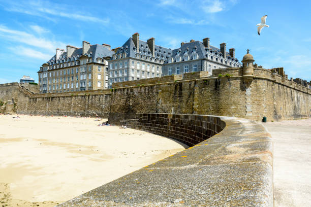 a cidade murada de saint-malo, frança, com edifícios residenciais de granito saliente acima da muralha e gente tomando sol na praia mole ao pé do muro alto. - bailey - fotografias e filmes do acervo