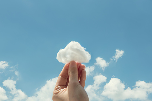 Woman hand holding cotton wool on cloud sky background. The development of the imagination, copy space.