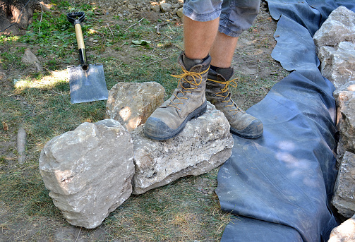 Lifestyle...This interesting close up shot, shows the feet and boots of a construction worker, with some decorative stone and equipment, that he will be using for a landscaping project. A possible metaphorical image, for manual labor.