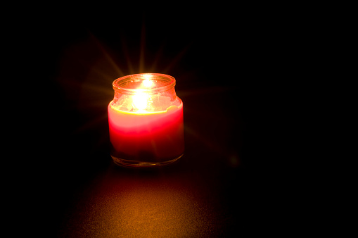 Red candle with warm rays.  Background is black (studio shot).