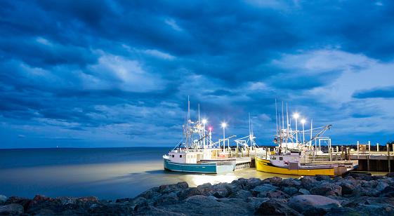 Fishing boats moored in Alma, Bay of Fundy, on the New Bruswick Atlantic coastline in Canada. Blue hour shot with dramatic clouds.