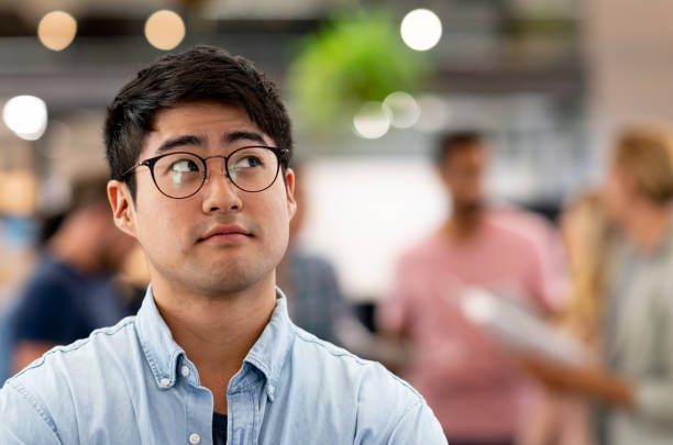 nachdenklicher asiatischen mann bei einem kreativ-büro - pensive business person looking up ideas stock-fotos und bilder