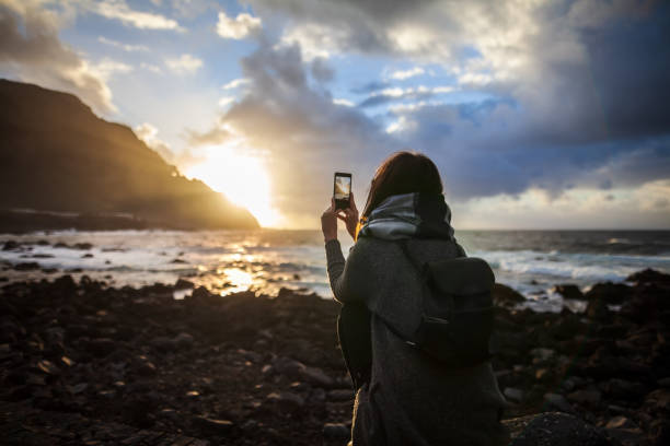 Young woman taking a photo of amazing sunset on Tenerife beach Young woman taking a photo with her phone of amazing sunset on Tenerife beach. Travel concept. Canary Island, Spain tenerife photos stock pictures, royalty-free photos & images