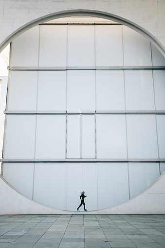 Symmetrical picture of woman running inside a big circle looking building. There's room for copy space.