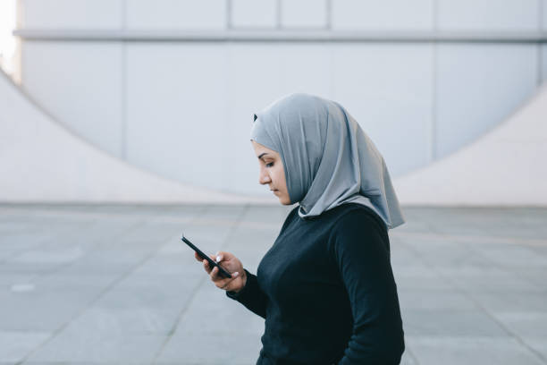 Portrait of muslim woman texting with her smartphone. Portrait of muslim woman texting with her smartphone. She's wearing a hijab. iranian ethnicity stock pictures, royalty-free photos & images