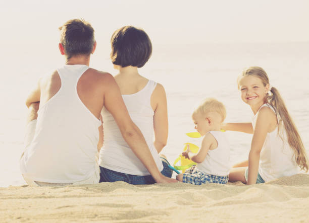 istock back view on family of four sitting on beach 999812338