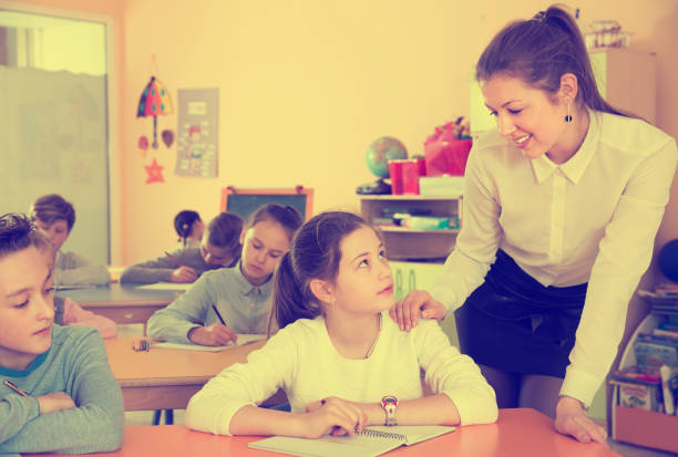 istock Children sitting at lesson in classroom, teacher helping 999817468