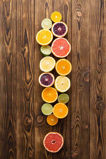 Overhead view of different sliced fruit in shape of exclamation mark on wooden background.