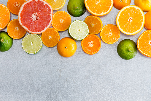 Mixed still life border of colorful fresh cut citrus fruit with oranges, grapefruit, clementine, lime and lemon on a textured grey white background with copy space