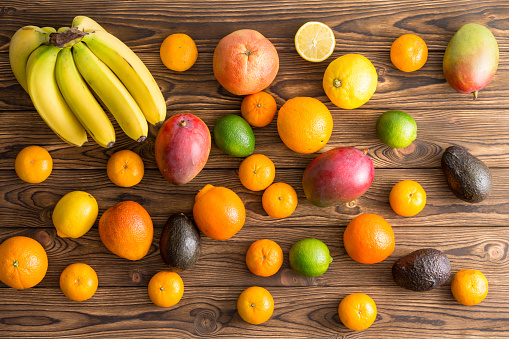 Scattered assorted fresh tropical fruit on wood for a healthy diet with bananas or plantains, mango, orange, lemon, lime, avocado pear, clementine and mandarin