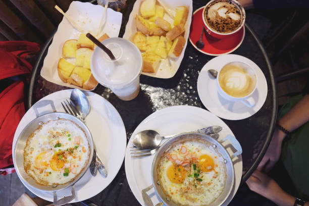 istock Typical breakfast with fried egg or pan omelet,Garlic bread and herb bread slice in white plate and Fried Fish balls with tomato sauce and cups of coffee on the table. 999828254