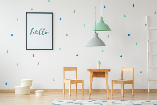 Lamps above wooden table and chairs in bright kid's room interior with poster on the wall. Real photo