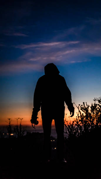 istock Man stands at horizon with camera as the sun sets 999859882