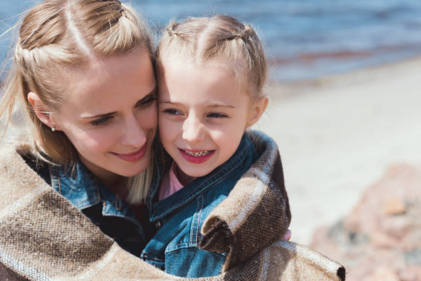 istock adorable daughter and mom hugging in blanket on sea shore 999865100