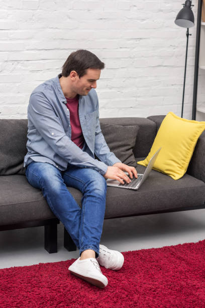 istock handsome adult freelancer using laptop on couch at home 999865568