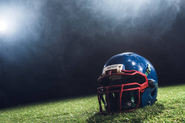 close-up erschossen, us-amerikanischer american-football-helm auf dem grünen rasen mit weißer rauch über - sportschutzbekleidung stock-fotos und bilder