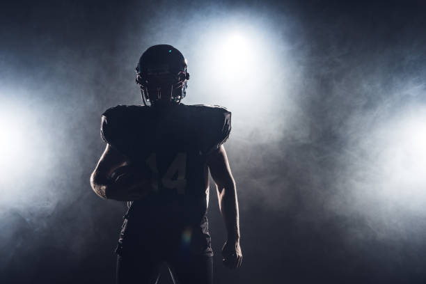 dunkle silhouette der ausgestatteten american-football-spieler mit ball gegen weißer rauch - football player american football athlete sport stock-fotos und bilder