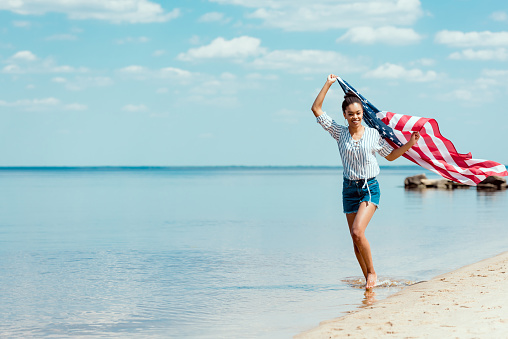 happy woman running in sea water with american flag, independence day concept