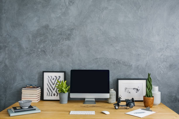 istock Plants, posters and computer desktop on desk in grey home office interior with copy space. Real photo 999877486