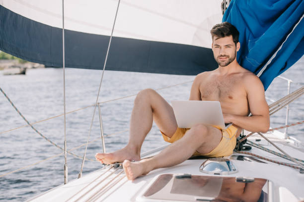 istock handsome shirtless man in swim trunks using laptop on yacht 999880206