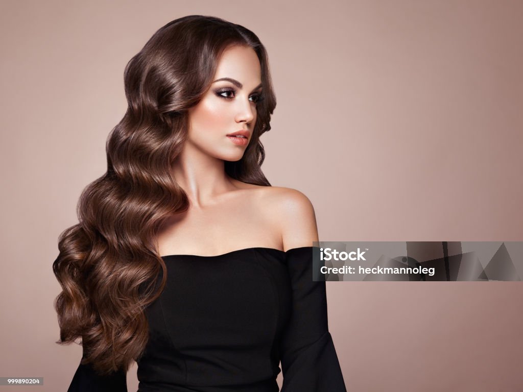 Brunette woman with curly hair Brunette Girl with Long Healthy and Shiny Curly Hair. Care and Beauty. Beautiful Model Woman with Wavy Hairstyle. Make-Up and Black Dress Fashion Model Stock Photo