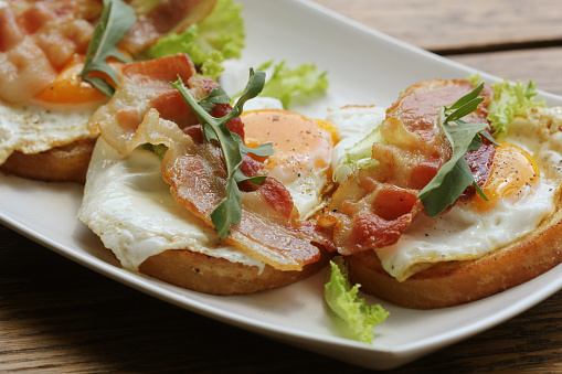 Bruschetta with rucola, chrispy bacon and poached egg served on white plate.