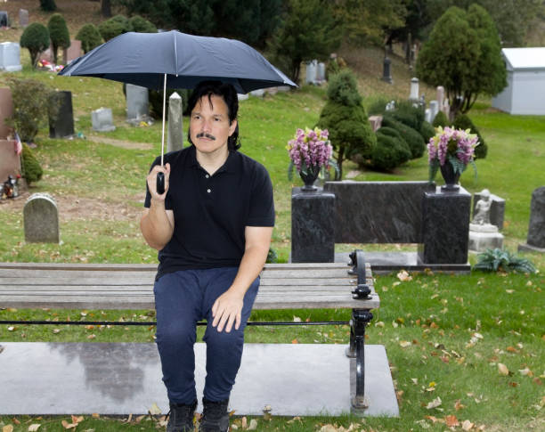 istock Hispanic man sitting with umbrella in cemetery 999922256
