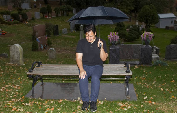 istock Hispanic man sitting on bench with lowered head in cemetery 999922278