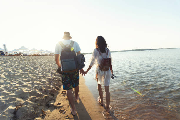 istock Two young people holding hands and walking on beach 999929948