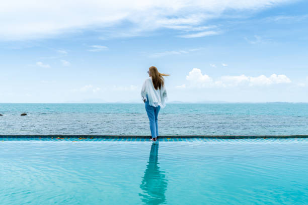 istock Women walk on beach pool at the seaside, cloud and blue sky is endless background, copy space. 999940412