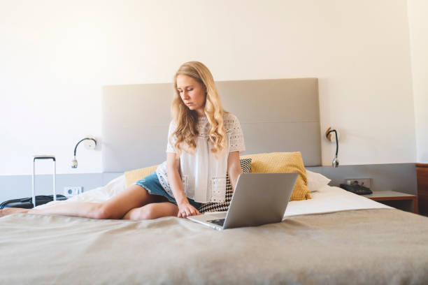 istock Beautiful young woman sitting on a bed, doing something on her laptop 999944128