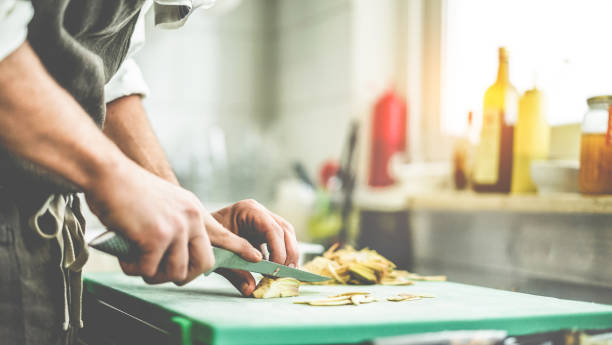 Chef cutting artichokes for dinner preparation - Man cooking inside restaurant kitchen - Focus on left hand - Vegan cuisine, lifestyle and healthy food concept