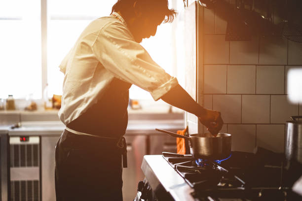 Male chef cooking in restaurant kitchen preparing  - Silhouette cook at work during dinner service - Italian style cuisine, lifestyle and healthy food concept - Focus on face