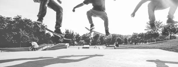 patinadores de saltar con patineta en deportes extremos de ciudad parque - chicos jóvenes skate realizando trucos y habilidades - y juventud concepto de estilo de vida - foco principal en el hombre izquierdo - blanco y negro edición - skateboarding skateboard park teenager extreme sports fotografías e imágenes de stock